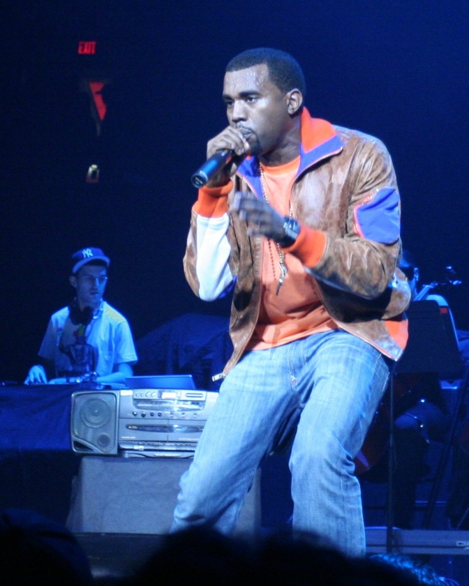 Kanye West in Lederjacke auf der Bühne. Er singt in ein Mikrophon.