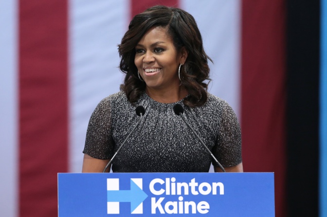 Michelle Obama steht lächeln an einem Rednerpult.