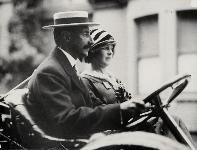 Schwarz-weiß-Foto eines Ehepaars in einem der ersten Autos. Beide sind elegant gekleidet.