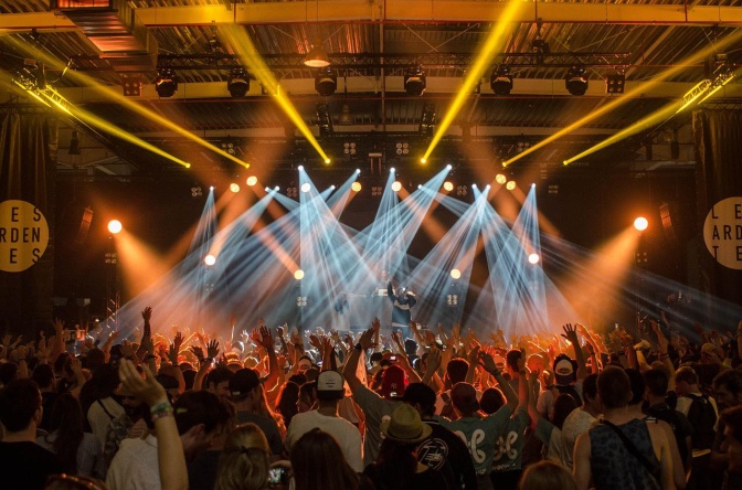 Das Publikum vor einer Bühne, auf der eine Band spielt. Der Raum ist von Strahlern in verschiedenen Farben beleuchtet.
