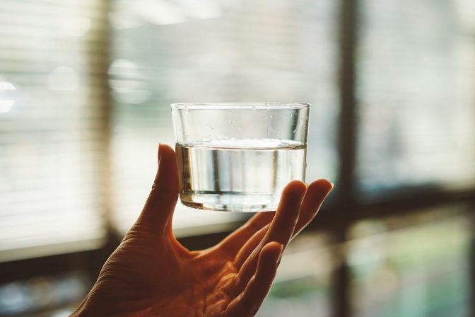 Eine Hand hält ein Glas mit Wasser.