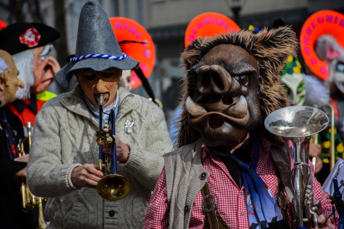 Ein Mann mit Trachtenhut und ein Mann mit Wildschweinmaske spielen Trompete. Sie tragen klassische Fastnachtskostüme aus dem Raum Freiburg.