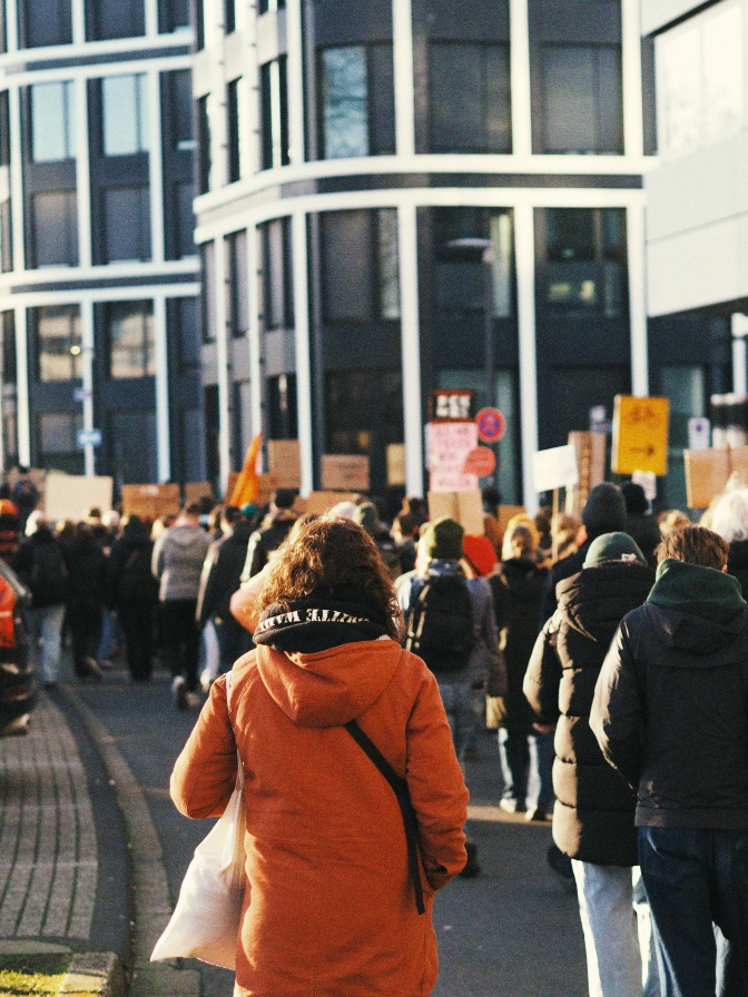 Menschen demonstrieren auf der Straße. Sie sind auf dem Bild nur von hinten zu sehen, die Demoschilder sind geblurred.
