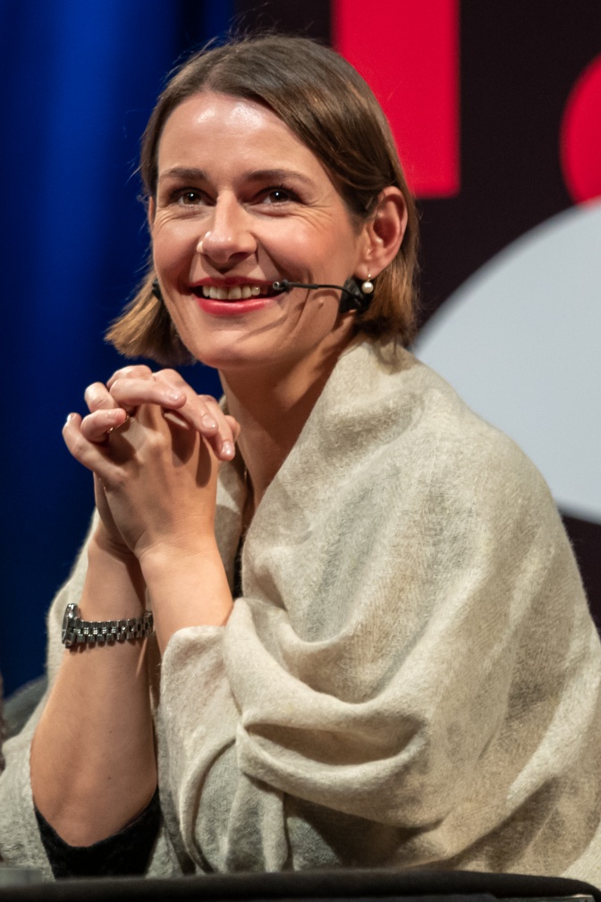 Annett Renneberg mit kinnlangen glatten Haaren in einer cremefarbenen Bluse. Sie hat die Hände gefaltet und lächelt in die Kamera.