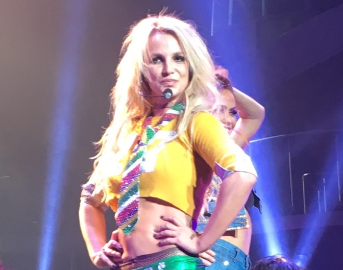 Britney Spears auf der Bühne in einem Coop Top und mit bunter, glitzernder Krawatte.