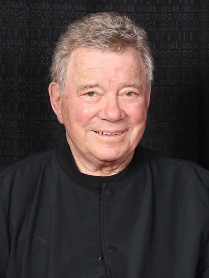 Portraitfoto von William Shatner in schwarzer Kleidung vor schwarzem Hintergrund.