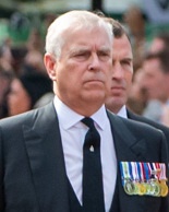Andrew Mountbatten-Windsor mit grauen Haaren und ernstem Blick. Er trägt Anzug und Krawatte und viele Orden am Revers.
