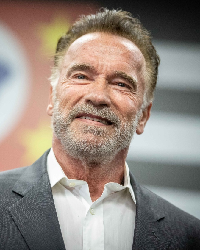Arnold Schwarzenegger mit grauem Vollbart iN Sakko und Hemd.