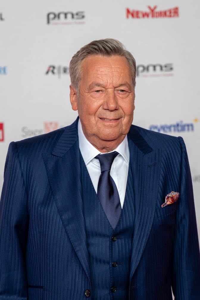 Roland Kaiser in einem blauen Anzug vor einer Logowand. Er lächelt in die Kameras.