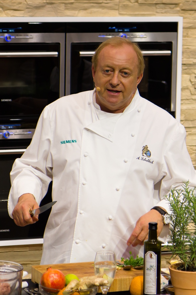 Alfons Schuhbeck in einer weißen Kochjacke. Er steht in einer Küche und spricht.