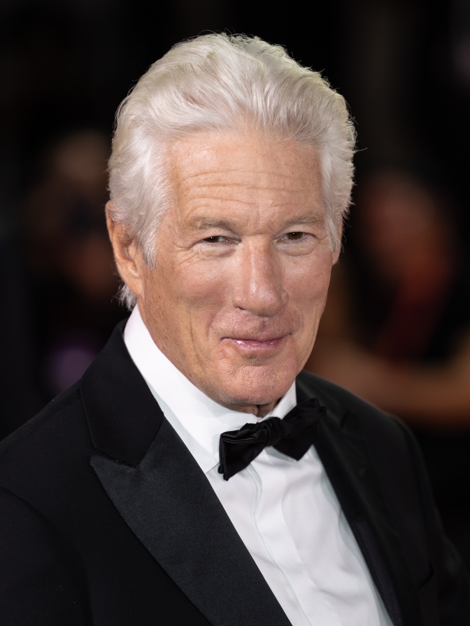 Richard Gere mit weißen Haaren in Anzug und Fliege. Er lächelt.