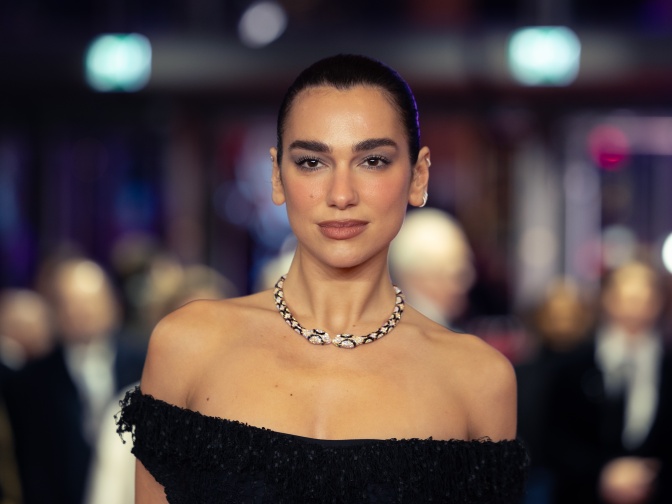 Dua Lipa in einem schulterfreien Kleid und mit einer Halskette in Schlangenform. Die Haare sind streng aus dem Gesicht frisiert.