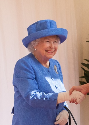 Die Queen in einem blauen Kostüm mit passendem Hut. Sie schüttelt jemandem die Hand.