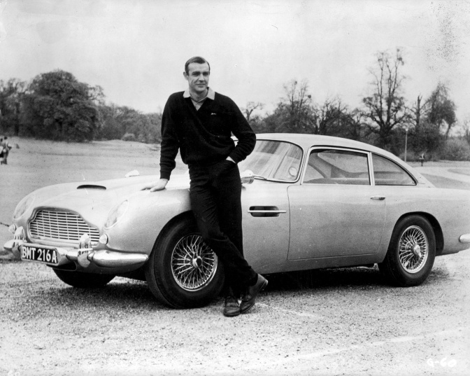 Schwarz-weiß-Foto von Sean Connery vor einem Sportwagen.