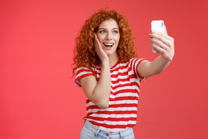 Eine junge Frau mit roten Locken filmt sich selbst mit dem Handy.