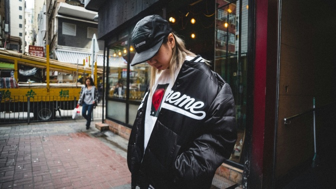 Ein asiatischer Mann mit Basecap und in Streetwear steht vor einem Ladenlokal.