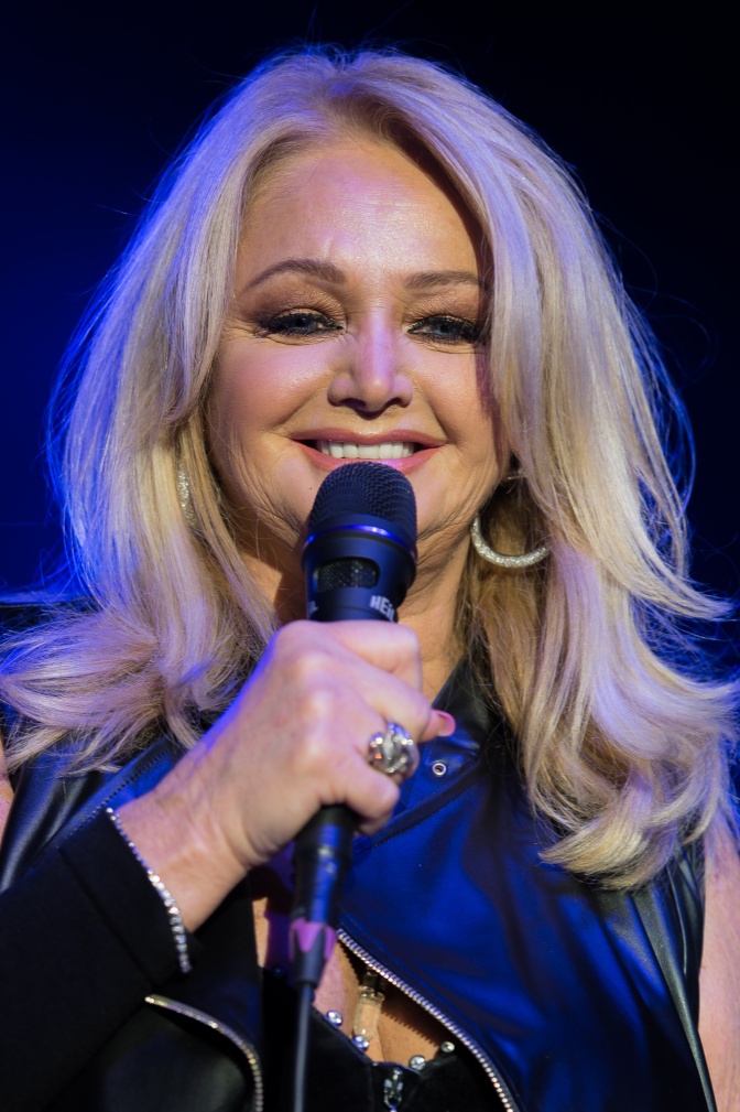 Bonnie Tyler singt lächelnd in ein Mikrofon.