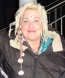 Gaby Köster mit blondierten zu kleinen Zäpfchen geflochtenen Haaren. Sie trägt eine schwarze Daunenjacke und hat sich einen Glitzerstein auf die Stirn geklebt.