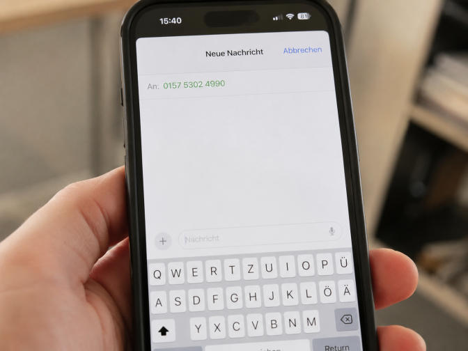 Eine Person hält ein Handy in der Hand und hat eine Telefonnummer eingegeben und eine neue Nachricht an diese Nummer geöffnet. Das Textfeld der Nachricht ist noch leer.