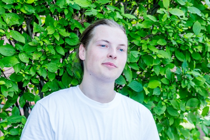 Gabriel Kelly in einem weißen T-Shirt vor einer Hecke.