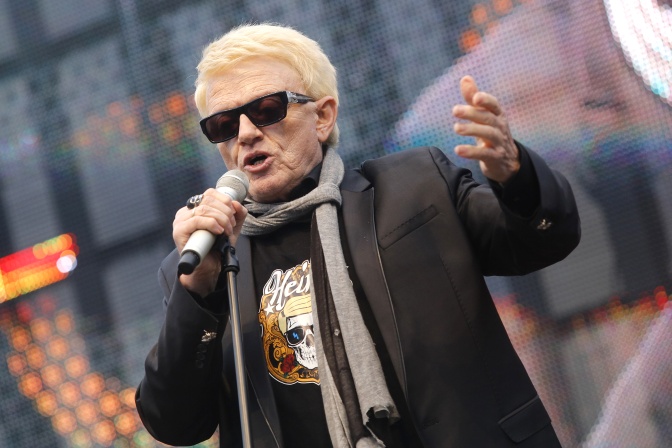 Heino mit schwarzer Sonnenbrille in Lederjacke auf der Bühne. Er singt in ein Mikro und gestikuliert mit den Armen.