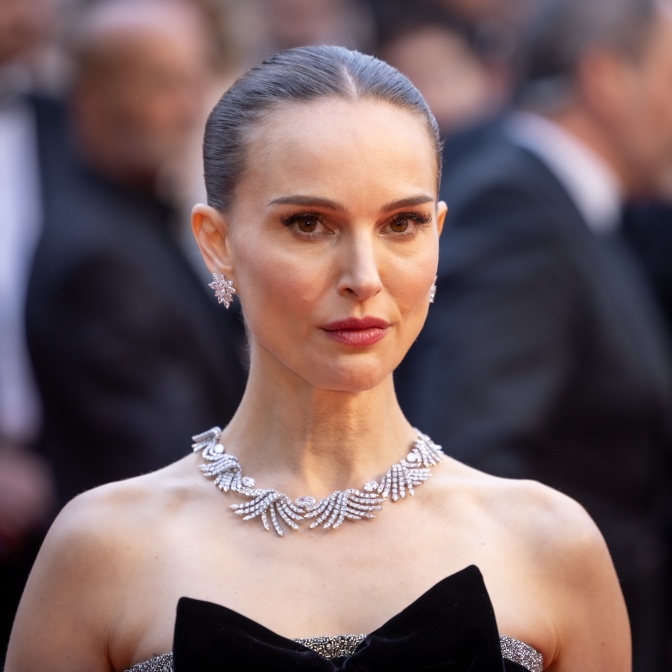 Natalie Portman in einem schulterfreien schwarzen Kleid mit viel Schmuck. Sie hat die Haare streng zurückgebunden und schaut ernst.