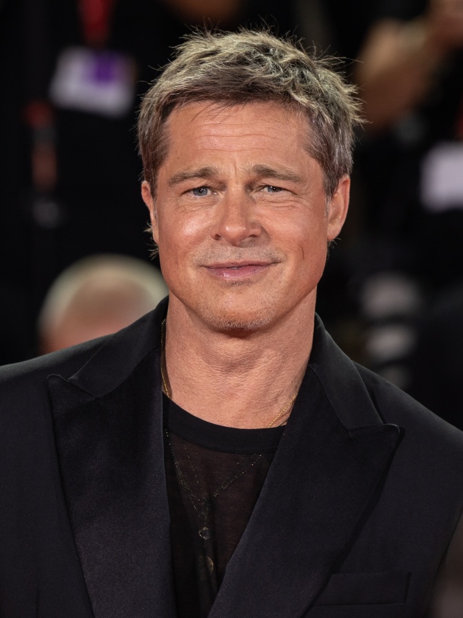 Brad Pitt in schwarzer Kleidung mit kurzen, dunkelblonden Haaren. Er lächelt und kneift die Augen zusammen.