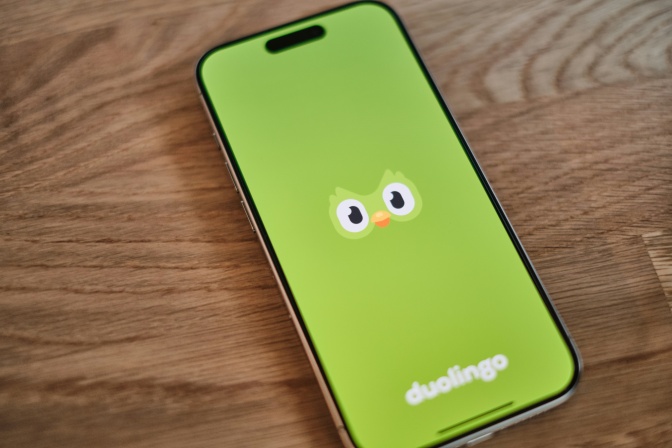 Die Duolingo-App ist auf einem Handy geöffnet. Man sieht die 2 Augen des Maskottchen-Vogels und den Schriftzug auf einem grünen Handydisplay.