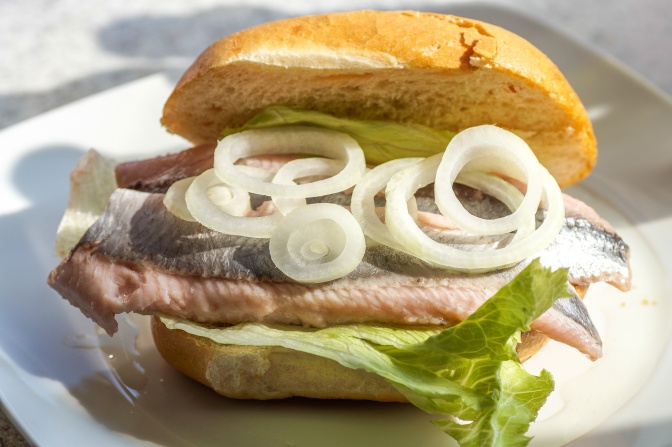 Ein Fischbrötchen mit Matjes, Salat und Zwiebeln