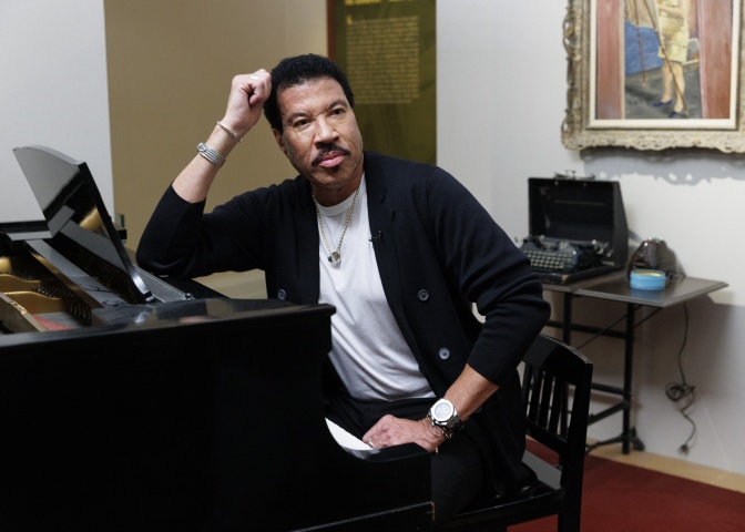 Lionel Richie sitzt am Klavier und stützt seinen Kopf auf den Arm. Er schaut direkt in die Kamera.