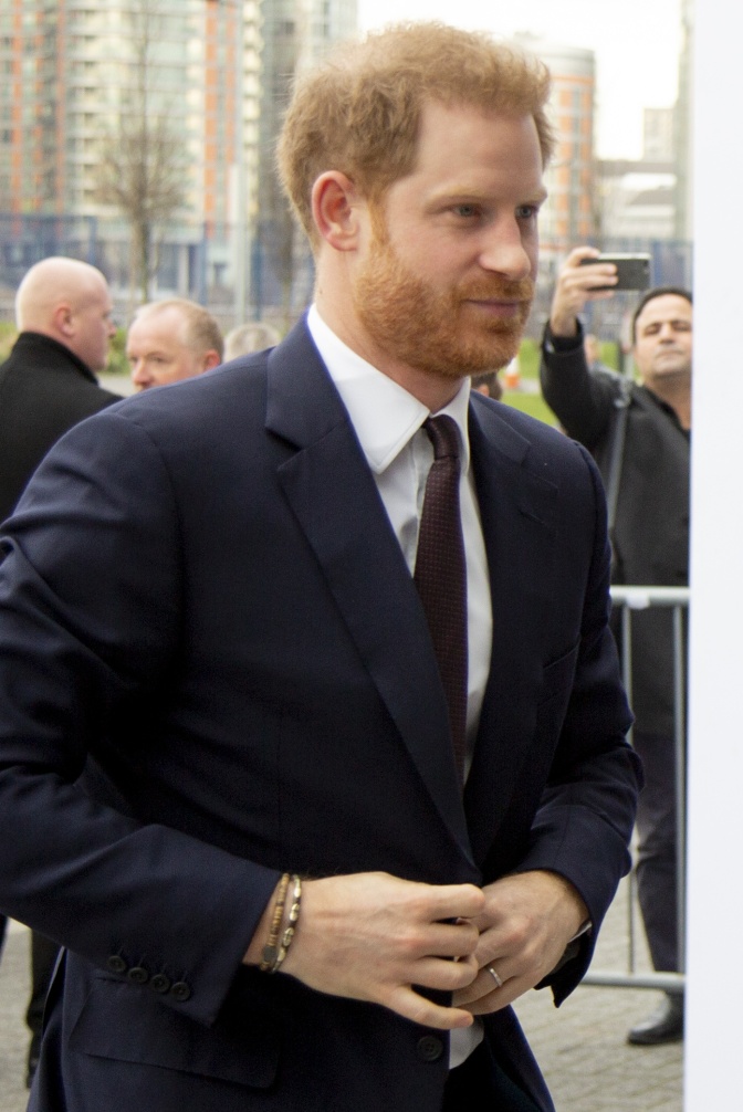 Prinz Harry in einem blauen Anzug mit Krawatte. Er hat die Hände vor dem Bauch gefaltet.