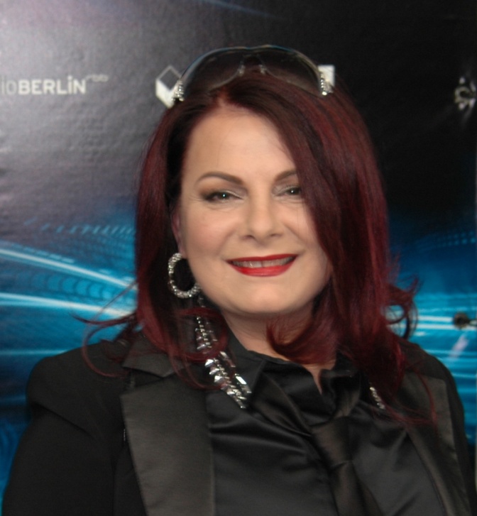 Marianne Rosenberg mit Bühnenmakeup in einem schwarzen Outfit. Sie lächelt in die Kamera.