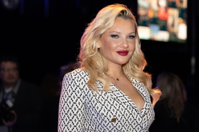 Evelyn Burdecki in einem tief ausgeschnittenen schwarz-weißen Blazer. Sie ist stark geschminkt und hat ihre blonden Haare in Wellen gelegt.
