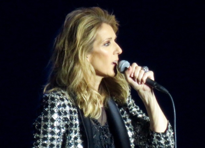 Céline Dion im Seitenprofil mit offenen Haaren. Sie singt in ein Mikrofon.