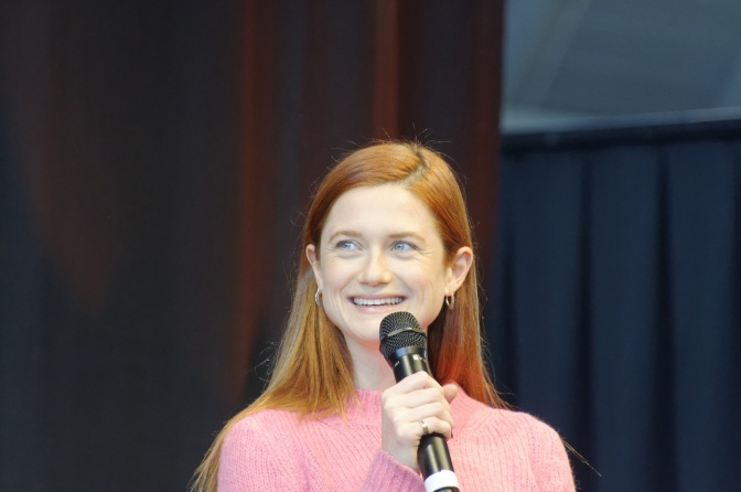 Bonnie Wright sitzt auf einer Bühne und spricht lächelnd in ein Mikrofon.