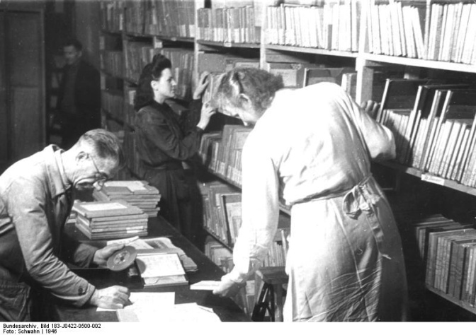 Schwarz-weiß-Foto von 2 Frauen und einem Mann, die alte Tonbänder sortieren und in Regale einräumen.