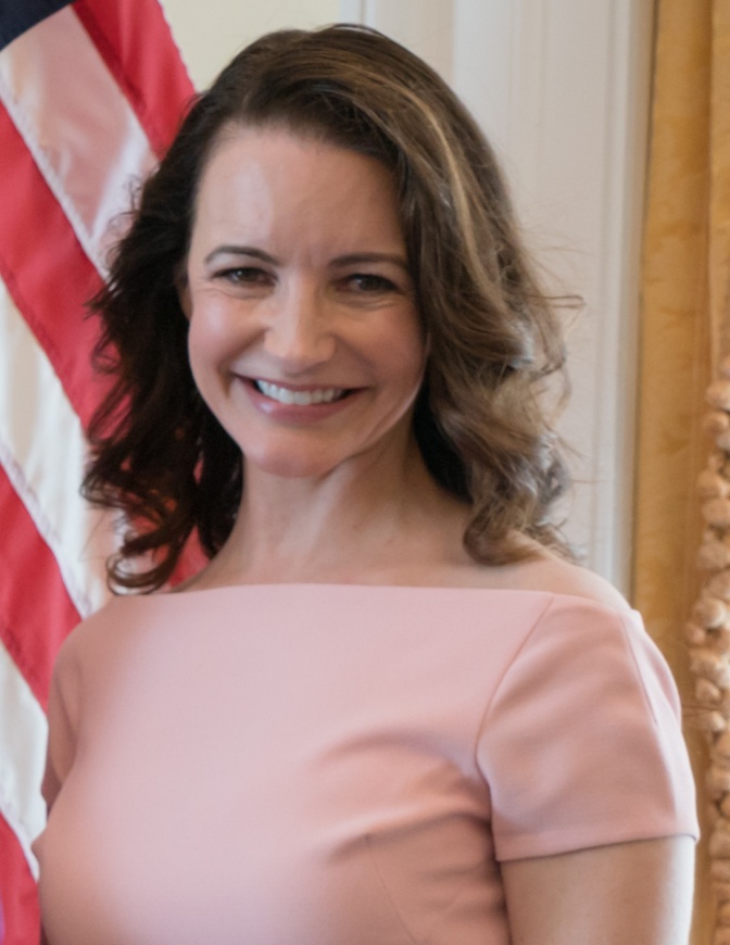 Kristin Davis steht in einem rosafarbenen Short lächelnd vor der amerikanischen Flagge.