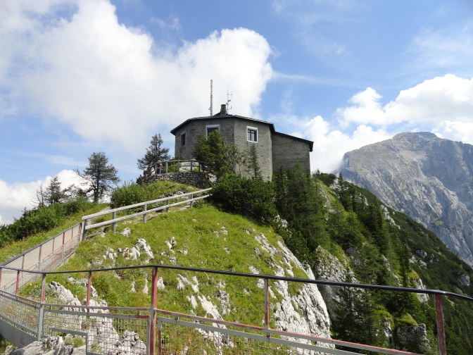 Ein grau verklinkertes Haus auf einem Berggipfel, darüber blauer Himmel.
