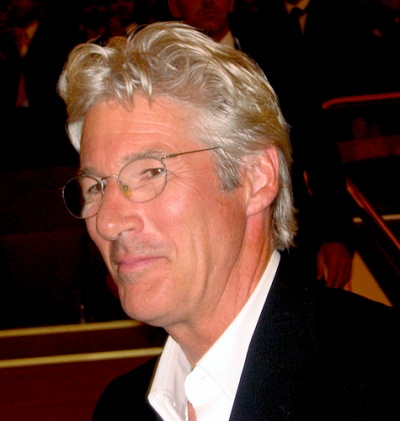 Richard Gere mit grauen, gewellten Haaren und Brille. Er trägt ein weißes Hemd mit Sakko.