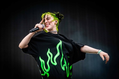 Billie Eilish auf der Bühne. Sie hat schwarz-grüne Haare und singt in ein Mikrophon.