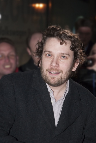 Christian Ulmen mit gewellten Haaren und Dreitagebart in einem schwarzen Sakko.