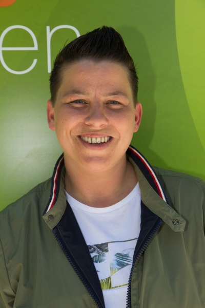 Kerstin Ott mit kurzenzur Tolle frisierten Haaren lächelnd vor einer Logowand