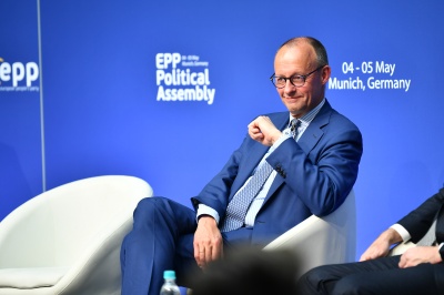 Friedrich Merz sitzt in einem Sessel vor einer Logowand auf der Bühne einer politischen Veranstaltung
