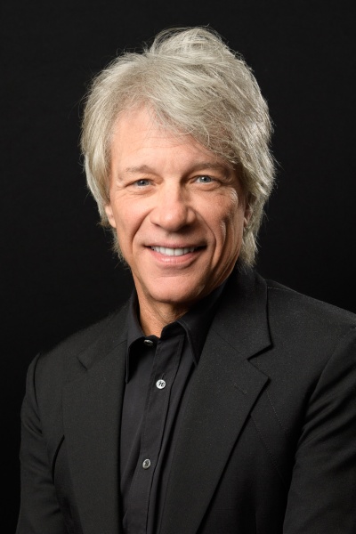 Jon Bon Jovi in einem schwarzen Hemd mit grauen Haaren. Er schaut lächelnd direkt in die Kamera.